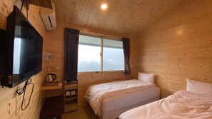 Habitación de cabaña de madera con una cama, un televisor, una ventana con cortinas y un escritorio pequeño con un hervidor.