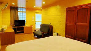 Habitación de hotel con cama, televisión, una silla, un armario de madera y ventana con cortinas.