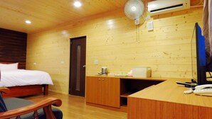 Een houten kamer met een bed, een bureau, een stoel, een ventilator en een airconditioner.