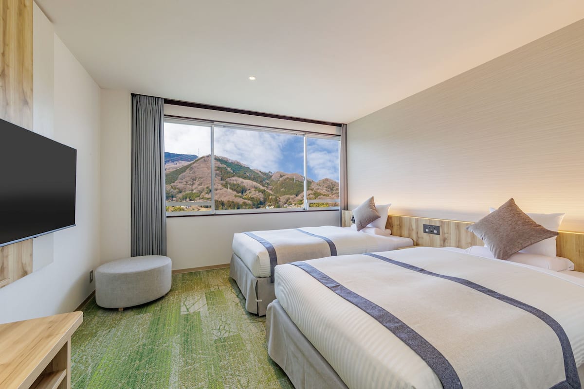 Une chambre d’hôtel avec deux lits, un téléviseur à écran plat, un petit coin salon et une grande fenêtre donnant sur les montagnes.