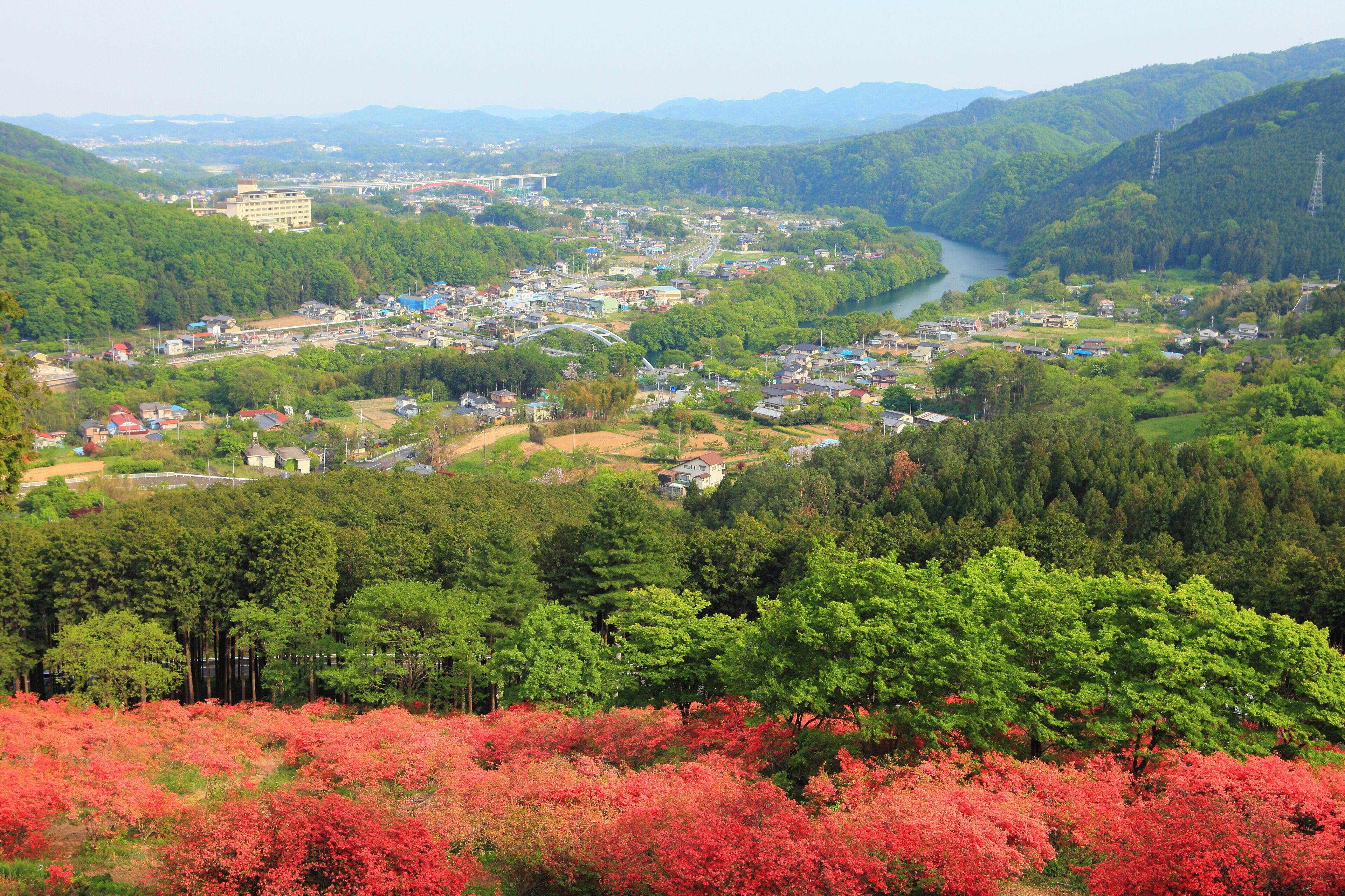 A town with a river, surrounded by green hills and red foliage.
