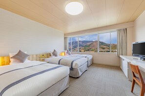 Une chambre d’hôtel avec deux lits, un bureau et une télévision. La chambre dispose d’une grande fenêtre donnant sur les montagnes.