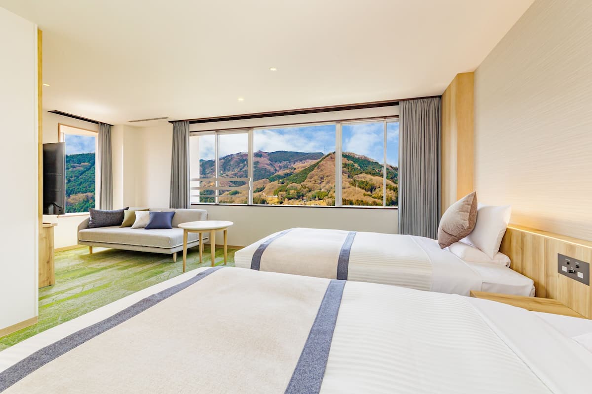 Une chambre d’hôtel avec deux lits, un canapé, une petite table et une grande fenêtre donnant sur la montagne.