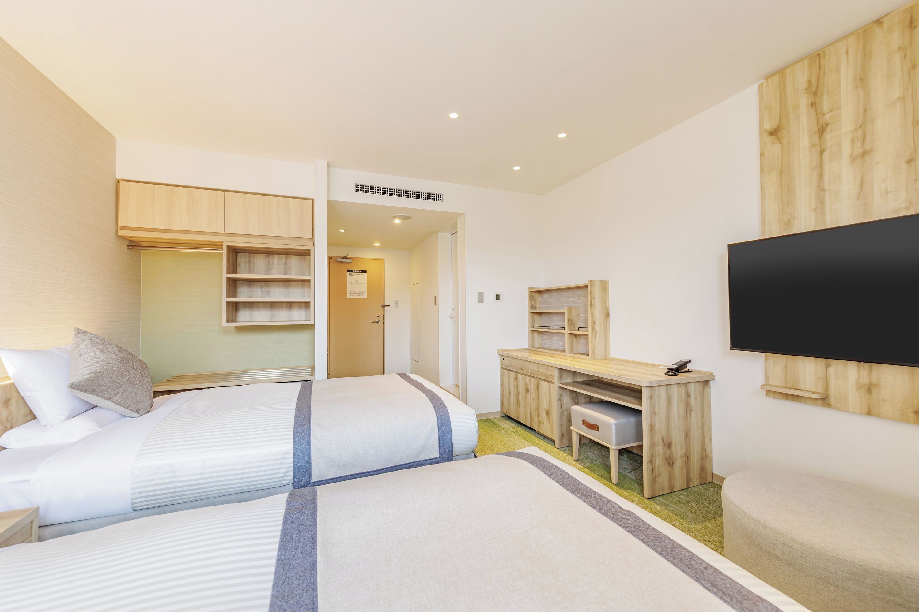 A modern hotel room with two beds, a desk, a television, and a wardrobe.
