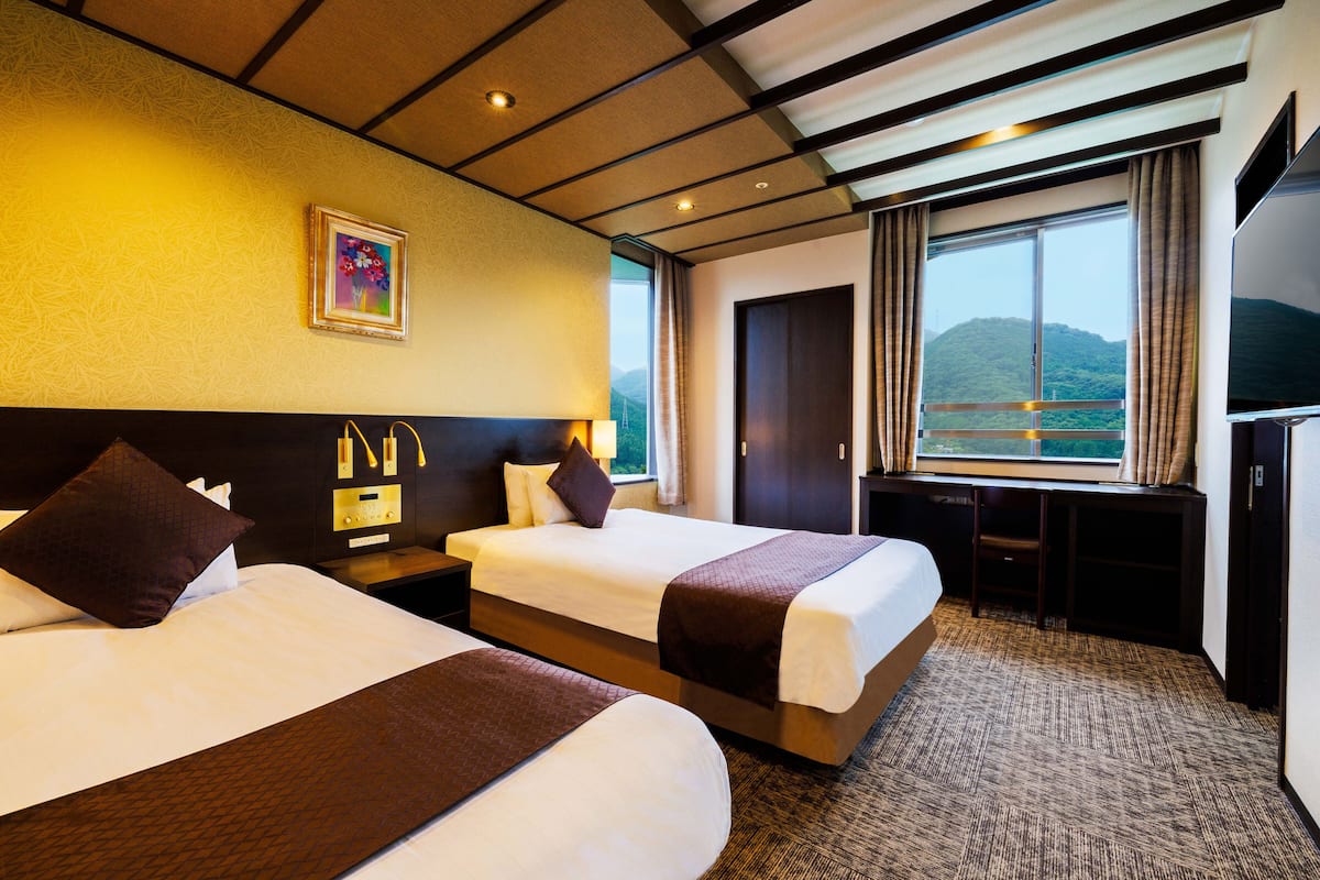 Une chambre d’hôtel avec deux lits, un bureau, une télévision et une grande fenêtre donnant sur la montagne.