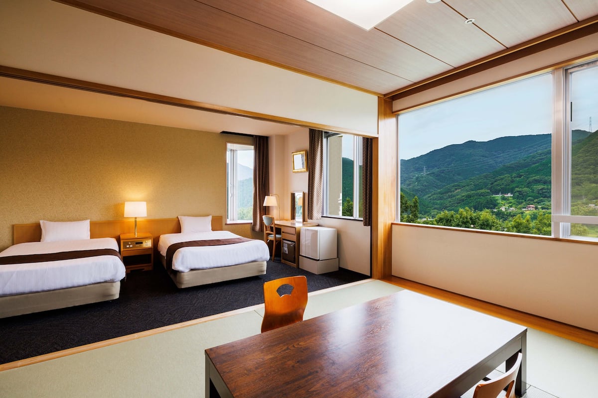 Une chambre d’hôtel avec deux lits, un bureau et une grande fenêtre donnant sur des collines verdoyantes.