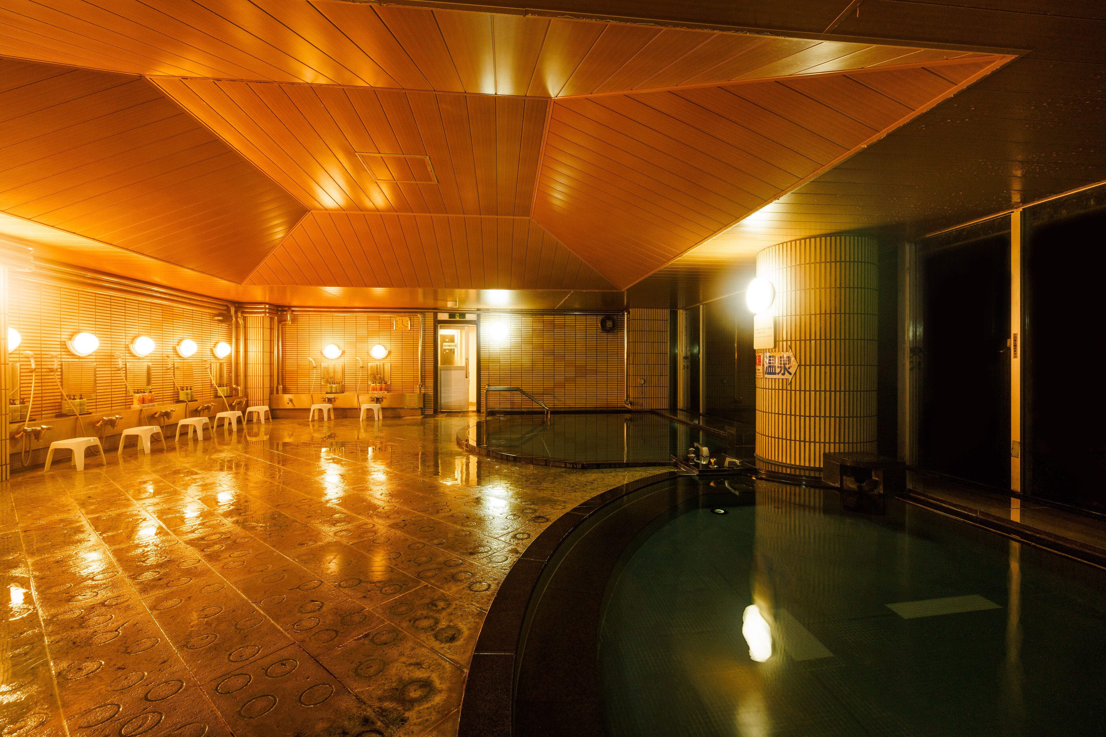 A spacious indoor swimming pool with a wooden ceiling and tiled floor, surrounded by seating and a changing room.