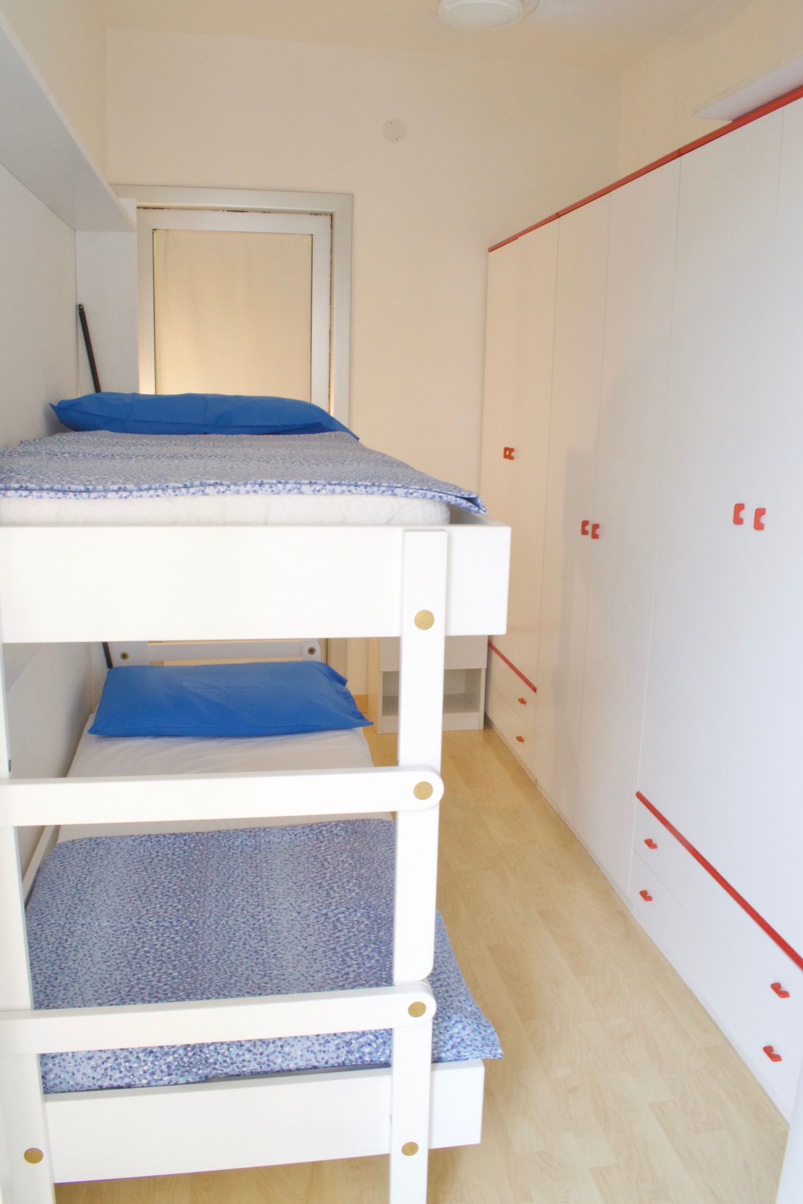 A bunk bed with blue bedding, a white wardrobe with red handles, and a wooden floor.