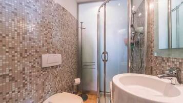Un baño con pared de mosaicos, inodoro, cabina de ducha de cristal y una bañera grande.