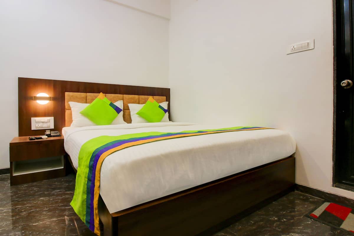 A hotel room with a bed, a nightstand, a wall-mounted light, and a door.
