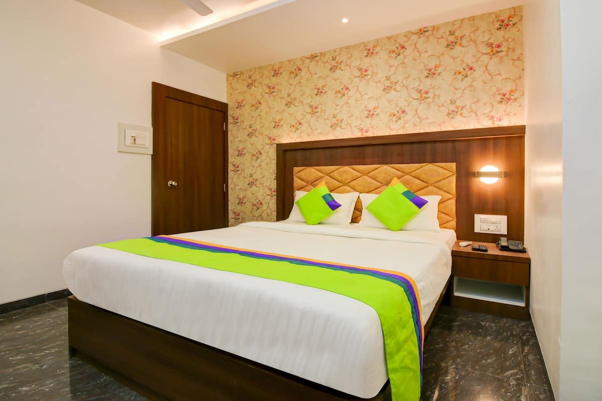 A hotel room with a bed, a nightstand, a wall-mounted lamp, and a door.