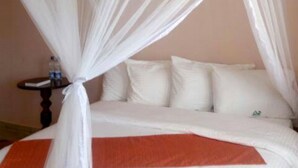 A bed with a white canopy and orange bedspread. - Great North Resort (Makuyu)