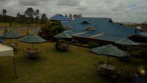 An outdoor patio area with tables and umbrellas, surrounded by buildings with blue roofs. - Great North Resort (Makuyu)