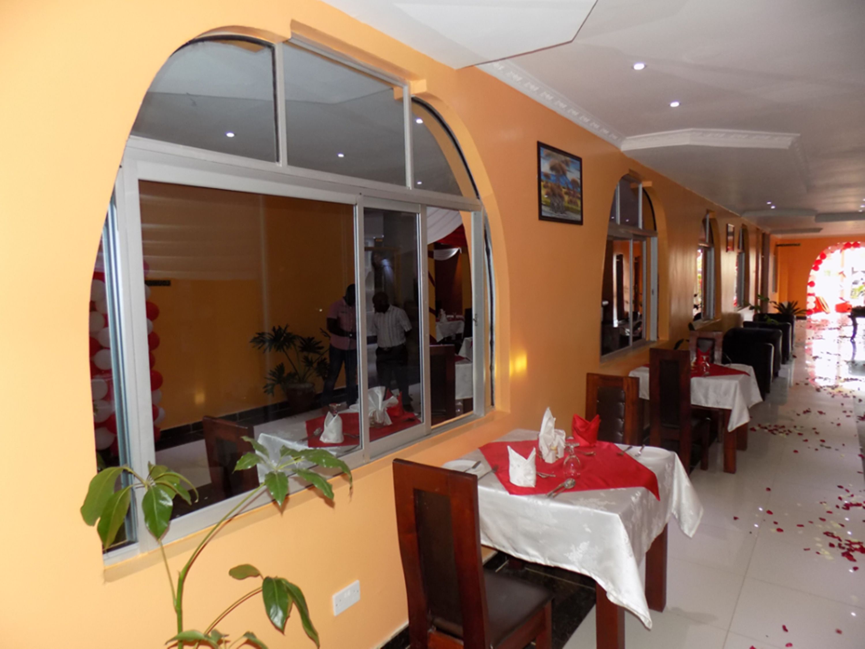 A restaurant with a long corridor, tables with white tablecloths, and red napkins.