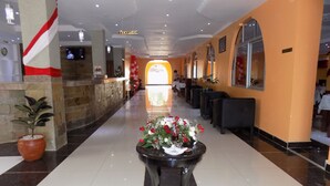 A hotel lobby with a reception desk, a reception sign, a reception area, a dining area with tables and chairs, and a potted plant. - Great North Resort (Makuyu)
