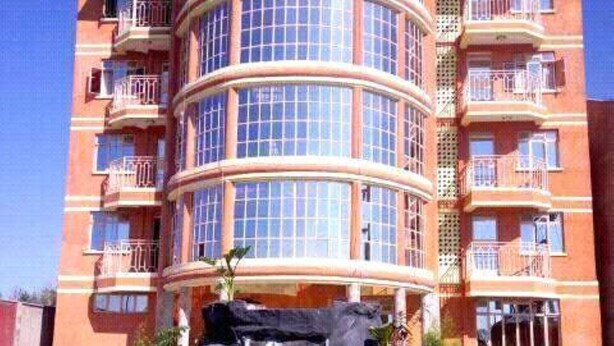 A multi-story hotel with a curved facade, balconies, and a rock formation with water in front. - Great North Resort (Makuyu)
