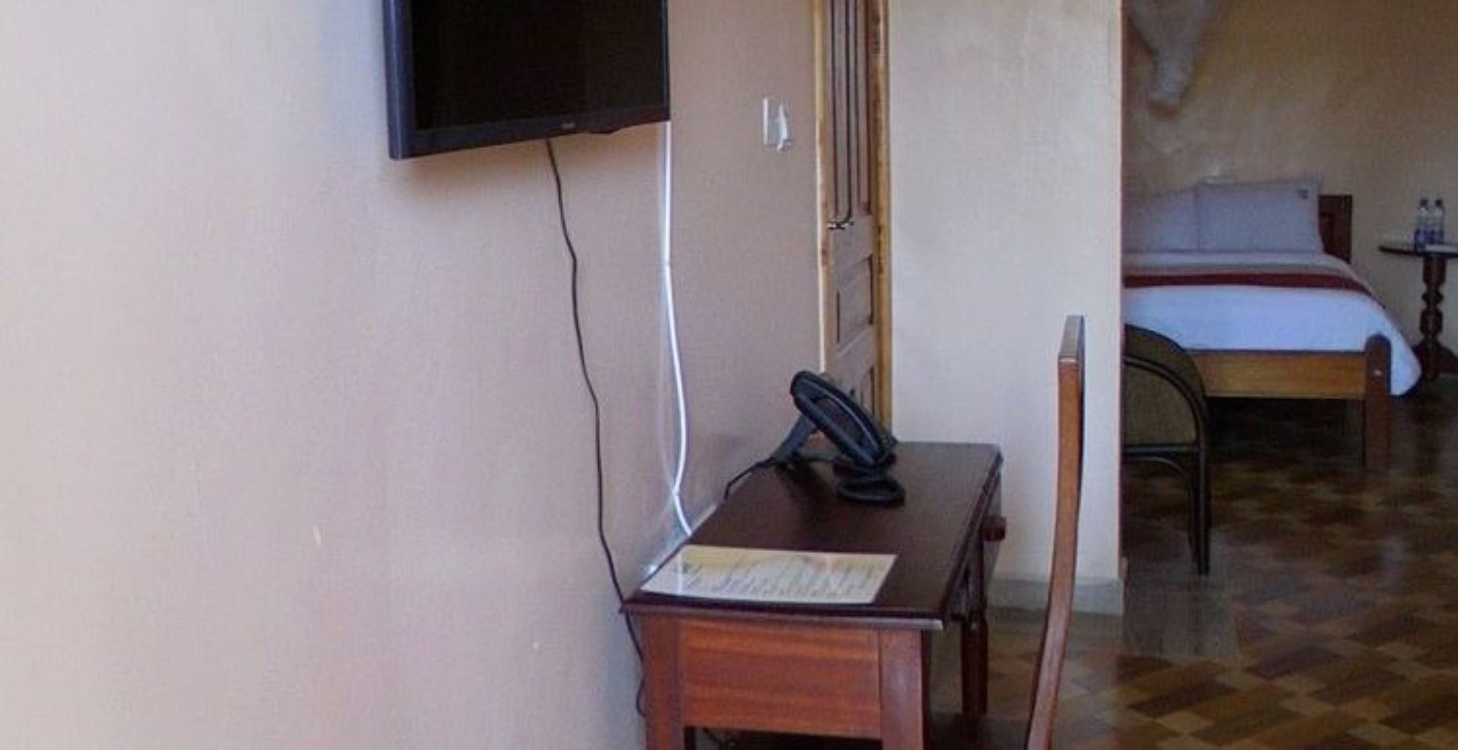 A room with a bed, a desk with a telephone, and a television mounted on the wall.