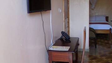 A room with a bed, a desk with a telephone, and a television mounted on the wall.