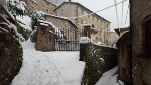 A snow-covered courtyard with a stone wall, a metal gate, and a building with multiple windows. - Affittacamere Ferrari (Pescaglia)