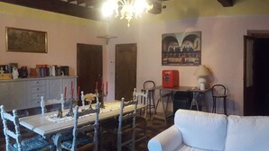A living room with a white sofa, a dining table with chairs, a fireplace, and a painting on the wall. - Affittacamere Ferrari (Pescaglia)