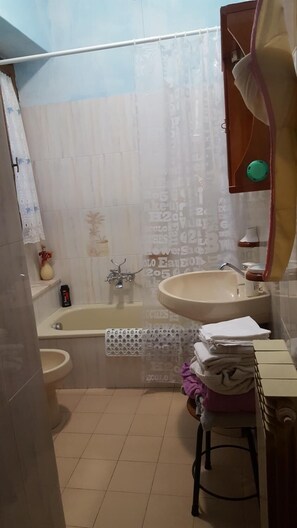 Un baño con bañera, lavamanos e inodoro. Hay un perchero con toallas y un pequeño estante con un adorno.