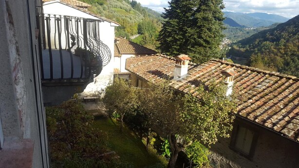 A traditional building with a tiled roof, surrounded by lush greenery and mountains in the background. - Affittacamere Ferrari (Pescaglia)