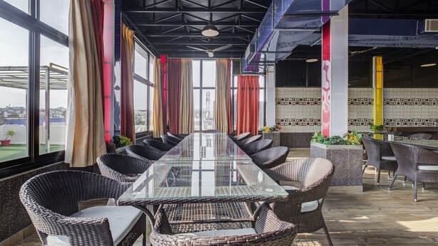 A conference room with a glass table and wicker chairs, large windows with curtains, and a view of the cityscape. - Treebo Trend Royal Dizire (Udaipur)