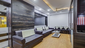 A modern living room with dark wood paneling, a leather sofa, and a glass coffee table. - Treebo Trend Royal Dizire (Udaipur)
