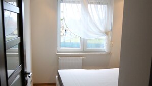 A bedroom with a single bed, a window with sheer curtains, a radiator, and a ceiling light fixture. - Apartament F&J 12 (Torun)