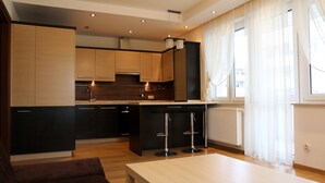 A modern kitchen with dark and light cabinetry, a central island, and a dining area with a table and two bar stools. - Apartament F&J 12 (Torun)