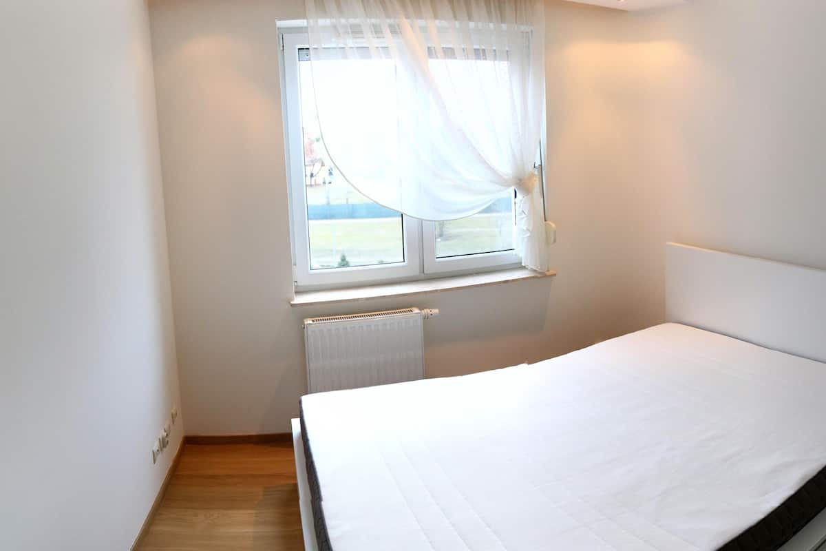 A bedroom with a single bed, a window with curtains, a radiator, and a wooden floor.