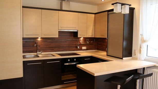 A modern kitchen with dark cabinetry, a stainless steel sink, and a built-in oven. - Apartament F&J 12 (Torun)