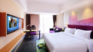 Habitación de hotel con una cama grande, un escritorio con computadora, un televisor montado en la pared y un mural con vista a la ciudad.