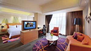 Habitación de hotel con cama, escritorio con televisor, sofá, mesa de centro y vistas al exterior.