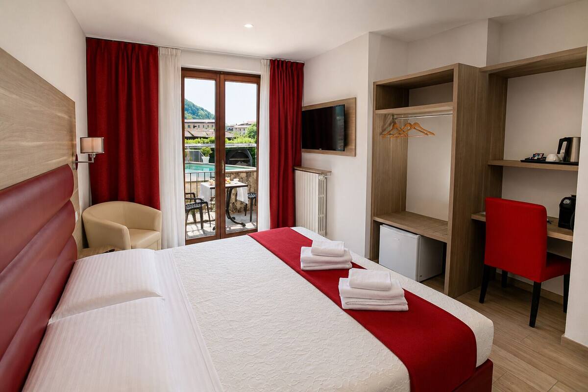 A hotel room with a bed, a desk, a chair, a TV, and a wardrobe.