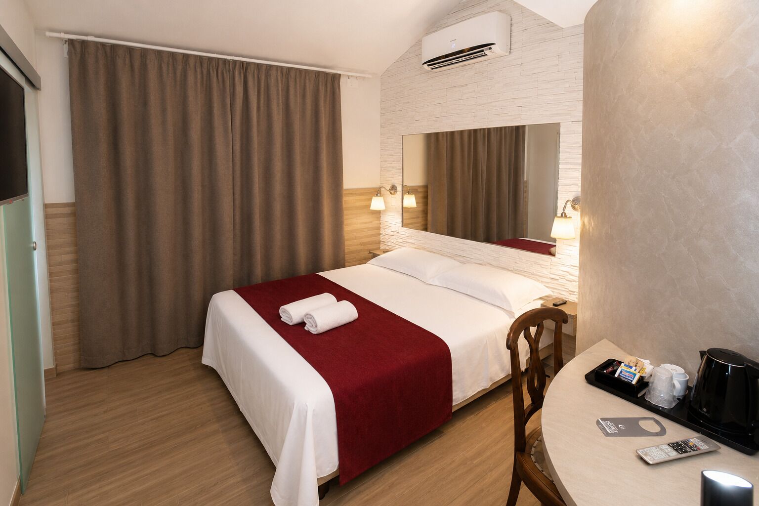 Una habitación de hotel con cama, una silla, una mesa con un control remoto, una cafetera y un espejo.