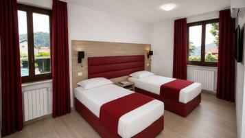 Quarto de hotel com duas camas, cabeceira de madeira, mesa de cabeceira, televisão fixada na parede e uma janela com cortinas.