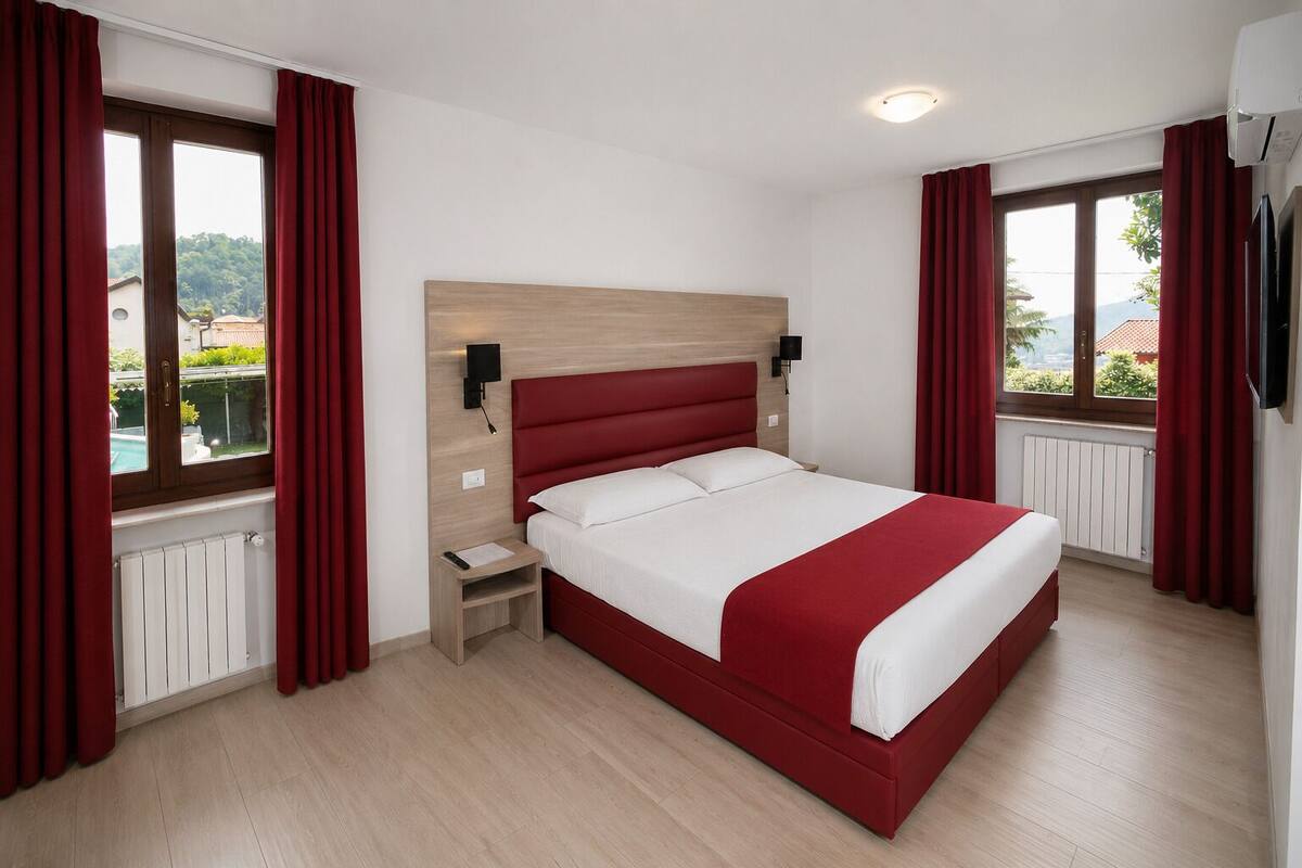 A hotel room with a large bed, wooden headboard, a nightstand, and a window with curtains.