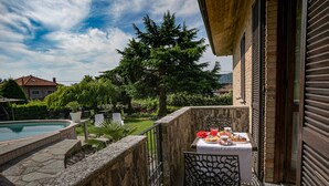 Un balcon avec une table préparée pour le petit-déjeuner, une piscine et un jardin avec des arbres et un hamac.