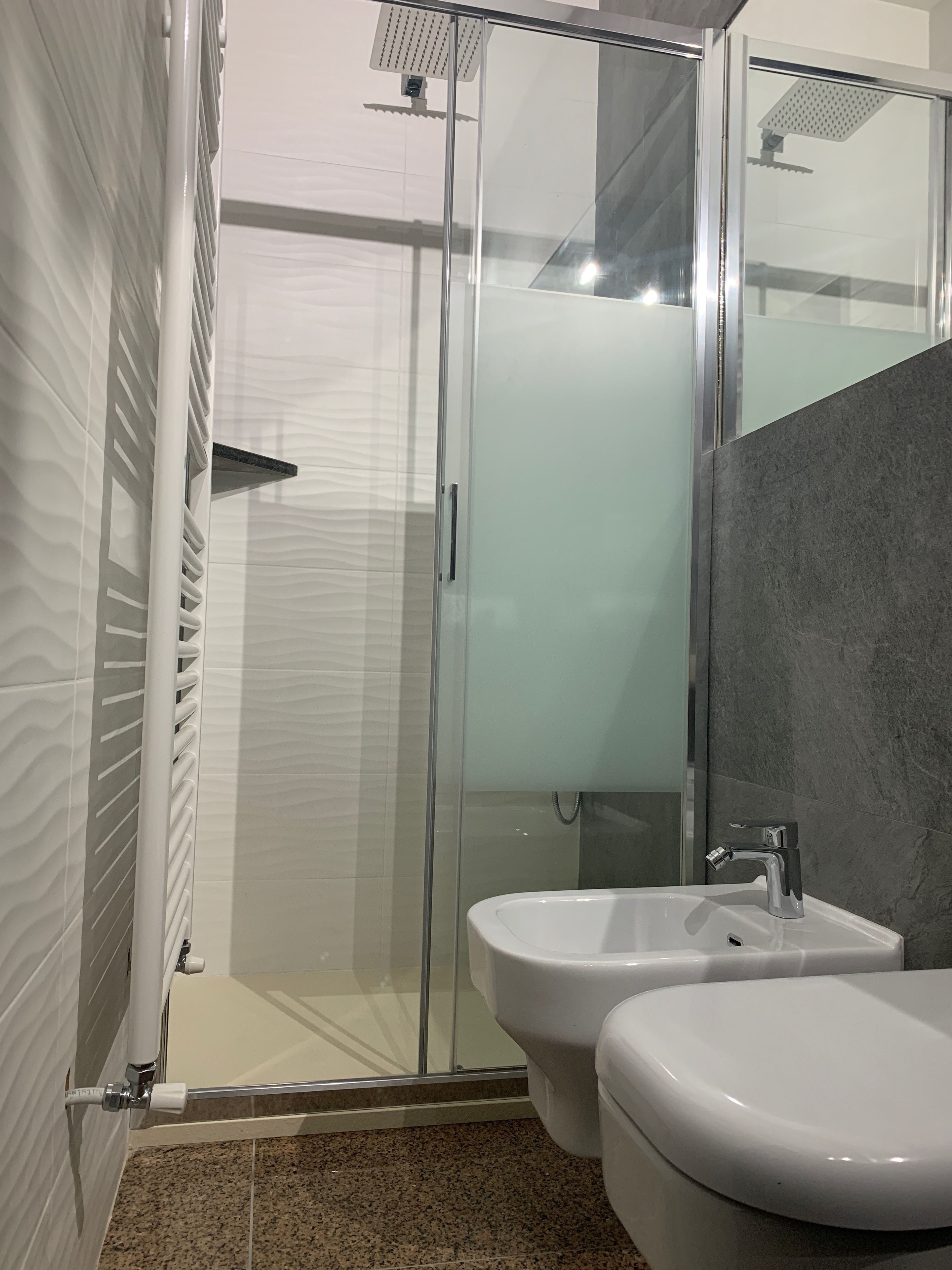 A modern bathroom with a glass-enclosed shower, two white sinks, and a marble-tiled floor.