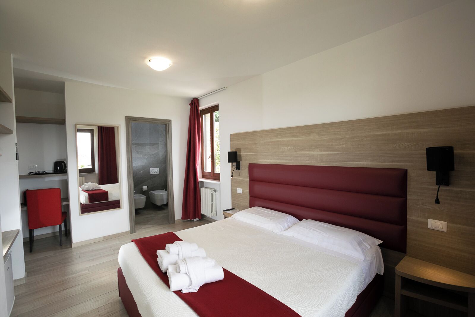Een hotelkamer met een groot bed, een bureau, een spiegel, een badkamer en een rood gordijn.