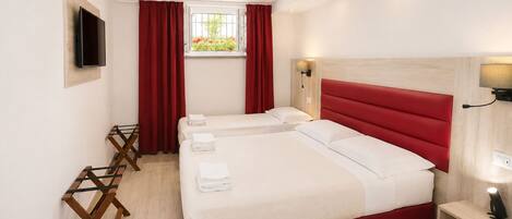 A hotel room with two beds, a TV, a window with red curtains, and a wooden floor.