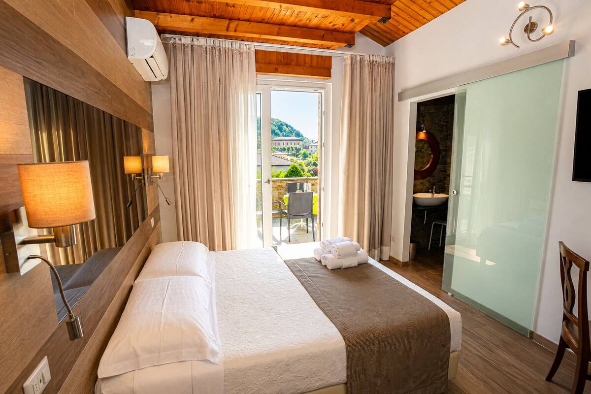 A hotel room with a bed, a bathroom, a view of the outside, and a wooden ceiling.