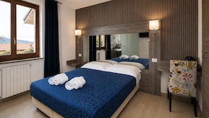 Une chambre d’hôtel avec un grand lit, un miroir, un mur lambrissé en bois, une fenêtre et une chaise à motifs floraux.