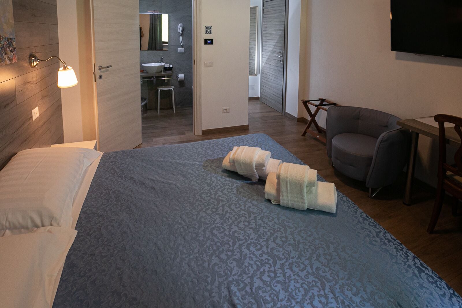 Une chambre d’hôtel avec un lit, un bureau, une chaise et une salle de bain visible à travers une porte ouverte.