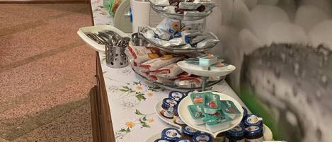 Une table de buffet garnie de divers plats et accompagnements, une pile d’assiettes blanches et un mur décoratif orné d’un tableau.