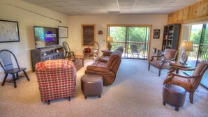 A cozy living room with a television, comfortable seating, and a view of the outdoors.