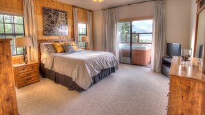 A bedroom with a bed, a wooden dresser, a desk, a television, and a sliding glass door to a balcony.