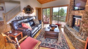 A cozy living room with a leather couch, a fireplace, and a balcony with outdoor furniture.