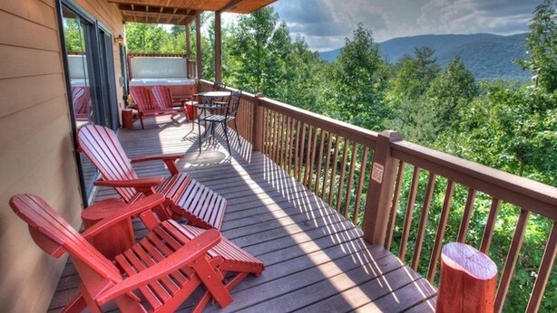 A wooden deck with Adirondack chairs and a table, overlooking a mountainous landscape.